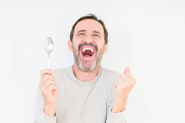 istock Senior man holding silver spoon over isolated background screaming proud and celebrating victory and success very excited, cheering emotion 1124670857