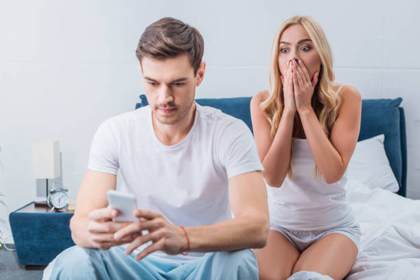 istock shocked young woman looking at boyfriend using smartphone on bed, distrust concept 1124672556