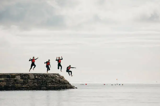 Group of teenage boys jumping into the sea from the pier.