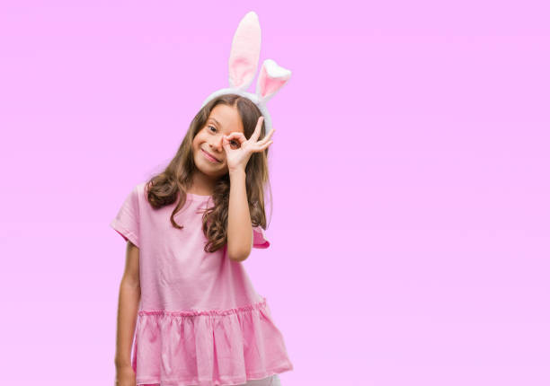 istock Brunette hispanic girl wearing easter rabbit ears with happy face smiling doing ok sign with hand on eye looking through fingers 1124675308