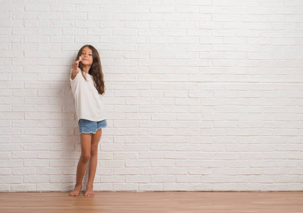 istock Young hispanic kid stading over white brick wall smiling friendly offering handshake as greeting and welcoming. Successful business. 1124676638