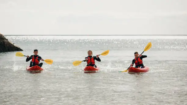Group of teenage boys kayaking, they're concentrating on their paddling and where they're going.