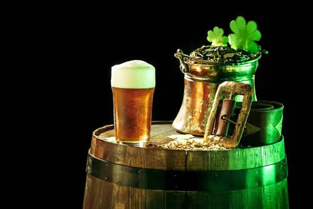 Photo of The wooden background with lots of gold coins and a large mug of beer with a green bow.