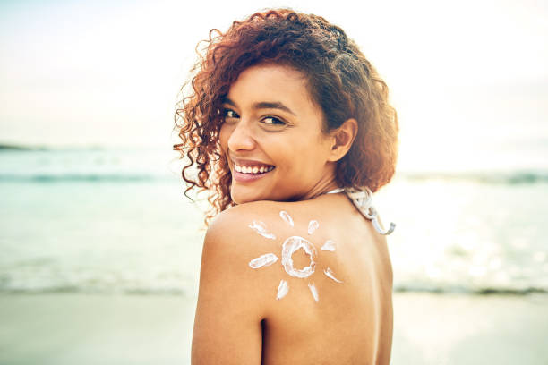 Make sure you're protected this summer Cropped portrait of an attractive young woman posing with sunscreen on her back at the beach suntan lotion photos stock pictures, royalty-free photos & images
