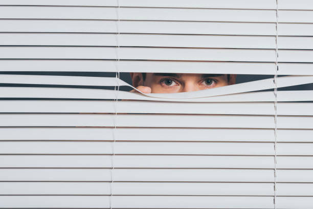 istock suspicious young man peeking and looking at camera through blinds, mistrust concept 1124692168