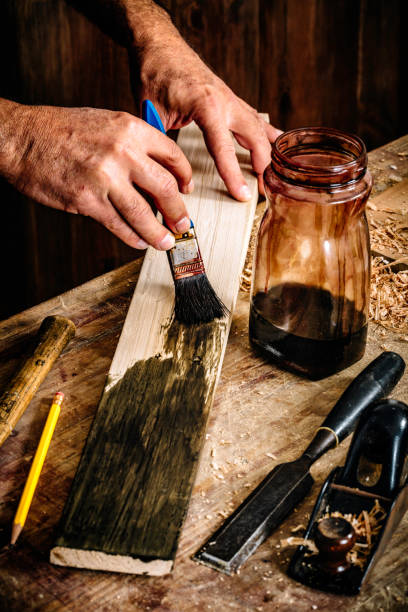 istock Mature carpenter hands painting on wood plank at home workshop 1124695557
