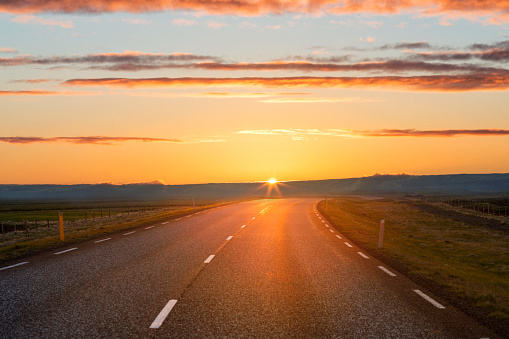 Scenic view of sunset over country road. Orange natural light is falling on Icelandic landscape. View of empty highway against sky.