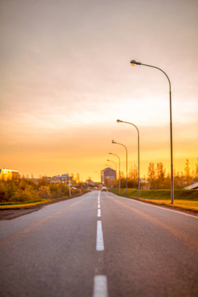 Surface level of empty road with street lights. Beautiful view of orange clouds over Iceland. Asphalt street in town during sunset.