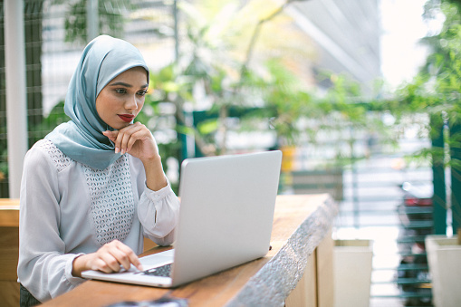 Beautiful woman sitting in sidewalk cafe, using lap top for work, wearing a hijab, Kuala Lumpur