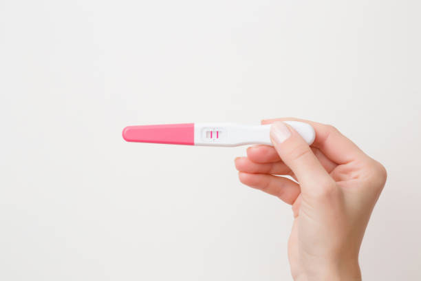 młoda kobieta trzyma rękę ciążowy test z dwoma paskami na szarym tle. wynik pozytywny. zbliżenie. rzut punktowy. puste miejsce dla tekstu. - pregnancy test zdjęcia i obrazy z banku zdjęć