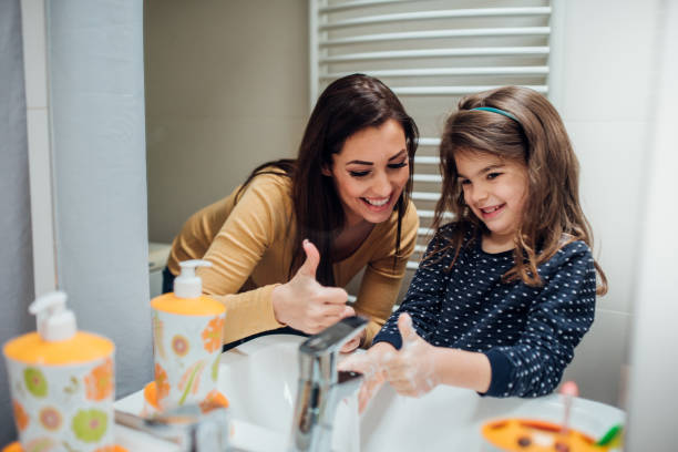 Woman helping daughter to wash hands