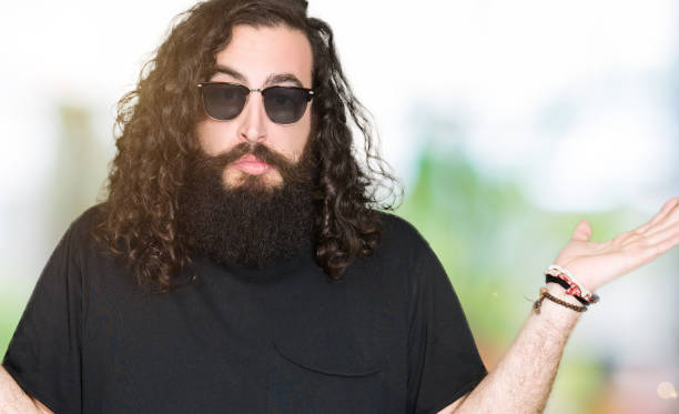Young hipster man with long hair and beard wearing sunglasses clueless and confused expression with arms and hands raised. Doubt concept. Young hipster man with long hair and beard wearing sunglasses clueless and confused expression with arms and hands raised. Doubt concept. shoulder tattoo designs for men stock pictures, royalty-free photos & images