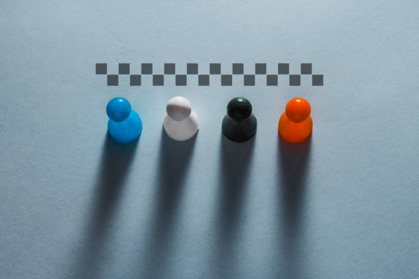 Group of four colored board game pawns lined up at the finish line stock photo