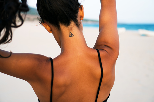 Horizontal photo of a beautiful girl walking at the beach. She has small tattoo at the neck