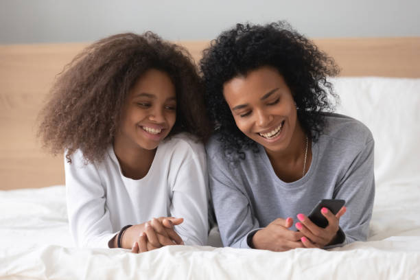 istock Smiling black mom and daughter relax with smartphone in bed 1124715237