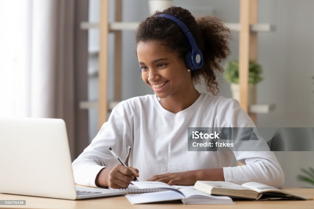 Feliz alumno negro auriculares haciendo la tarea de la escuela - Foto de stock de Adolescente libre de derechos