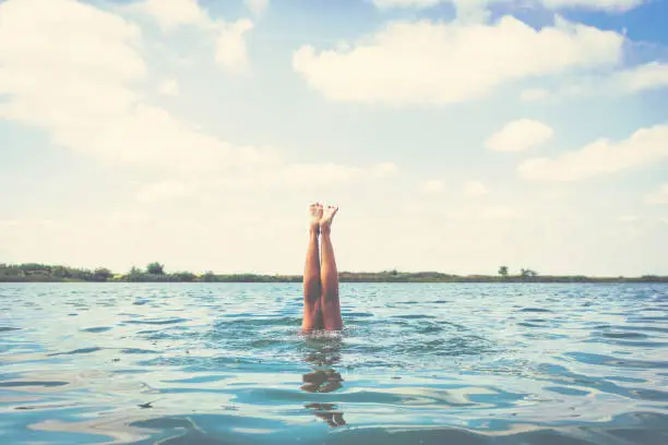 Woman's legs above the water. Unrecognizable woman diving in the sea. Copy space.