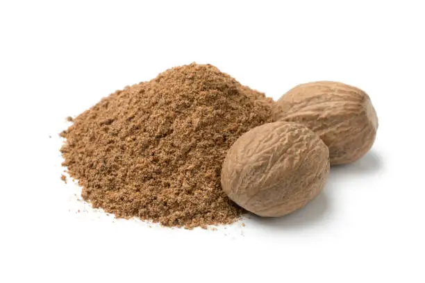 Heap of ground nutmeg and whole nutmeg seeds isolated on white background