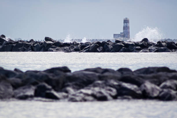 A lighthouse among the rocks and stormy sea waves in winter A lighthouse among the rocks and stormy sea waves in winter cielo minaccioso stock pictures, royalty-free photos & images