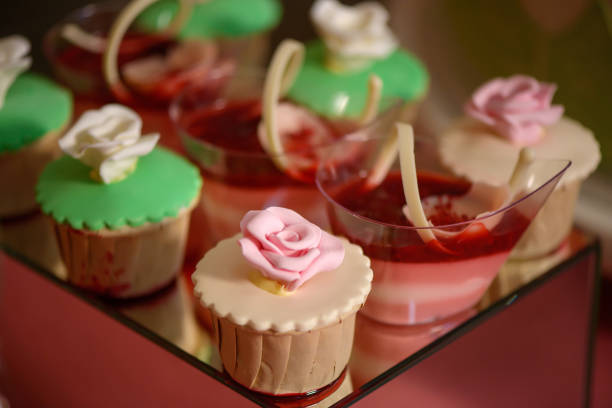 Close up of dessert assortment of playful or themed bite-sized cakes, fruit mousse, cupcakes, displayed on an elegant mirror cake stand, at a wedding reception, a birthday party or a formal event.