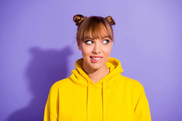 Close up photo of amazing beautiful brunette she her lady pretty Close up photo of amazing beautiful brunette she her lady pretty hairdo looking watching to empty space with wonder bite lower lip wearing casual bright yellow pullover isolated on purple background topknot stock pictures, royalty-free photos & images