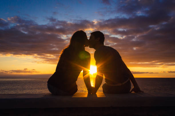 Man and woman sitting by the sea kissing at sunset at Meloneras beach walk, Gran Canaria Couple silhouette enjoying romantic colorful twilight. Valentines Day, honeymoon romantic date concepts love stock pictures, royalty-free photos & images