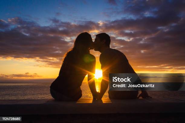 Foto de Homem E Mulher Sentada À Beiramar Beijando No Pôr Do Sol Na Caminhada Da Praia De Meloneras Gran Canaria e mais fotos de stock de Casal