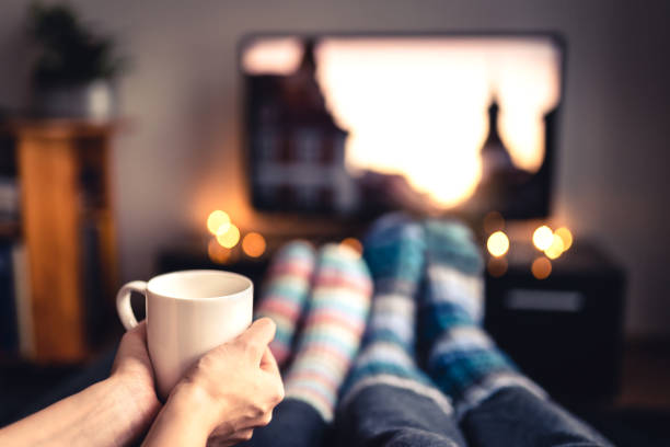 couple drinking tea, hot chocolate, eggnog or mulled wine and watching tv in warm cozy woolen socks in winter. woman holding cup of morning coffee in home living room. sick people with flu. - coffee cafe drinking couple imagens e fotografias de stock