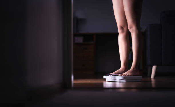 lady standing on scale. weight loss and diet concept. woman weighing herself. fitness lady dieting. weightloss and dietetics. dark late night mood. - weight scale dieting weight loss imagens e fotografias de stock