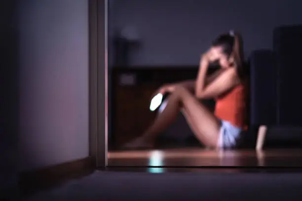 Sad teenager with smartphone in her room sitting on floor. Lonely teen girl crying with mobile phone. Harassment or online cyber bullying in social media or internet. Mean message or troll comment.