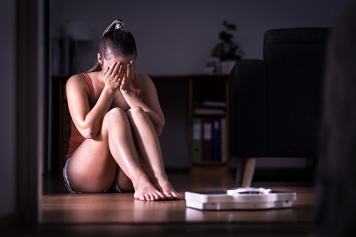 Mujer que tiene estrés sobre pérdida de peso, dieta o engordar. Comer desorden, anorexia o bulimia concepto. Jovencita llorando y sentada en el piso con la escala. photo