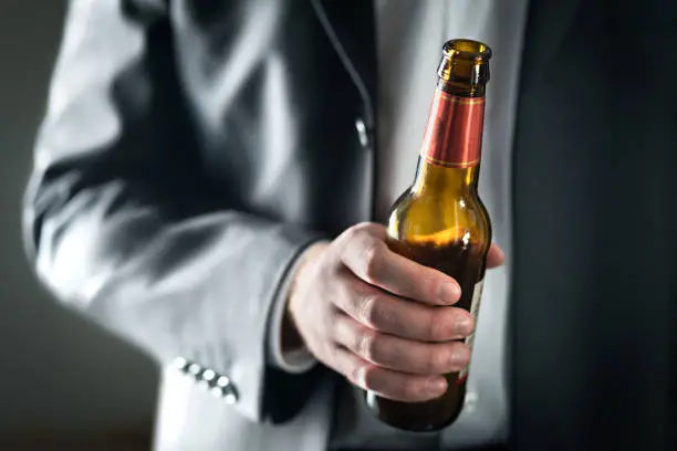 Photo of Business man drinking beer. Businessman holding bottle of alcohol. Drunk guy in suit with booze. Party at work or office. Celebration of success.