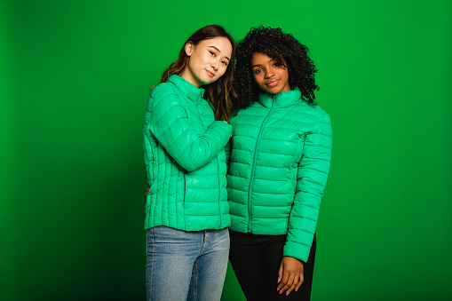 Two female friends standing infront of a green background in a studio.