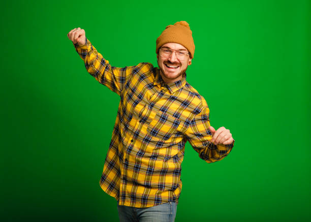 Mid adult hipster man dancing infront of a green studio background.