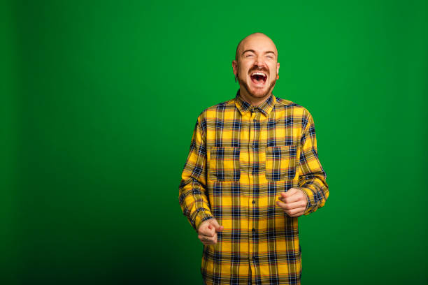 Mid adult man standing infront of a green background in a studio. He ecstatically laughing.