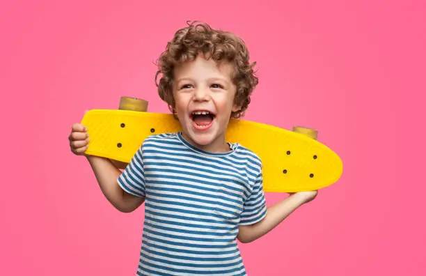 Photo of Happy curly boy laughing and holding skateboard