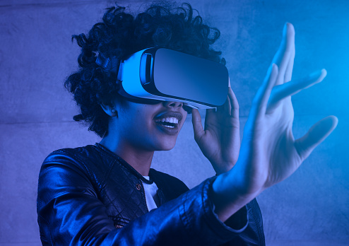 Surprised african american young woman touching experiencing VR helmet. Portrait toned in blue filter