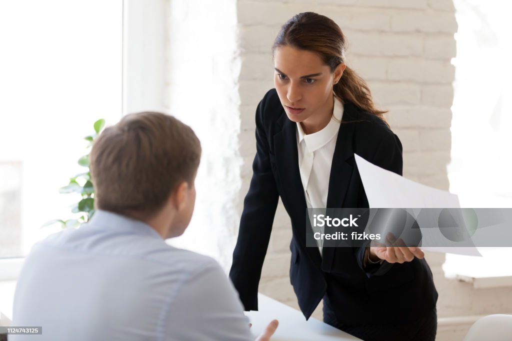 Serious businesswoman blaming employee for mistake in paper document Serious businesswoman blaming employee for mistake in paper document, financial report, dissatisfied woman, ceo, team leader arguing with worker about bad work results, failure, business problem Conflict Stock Photo