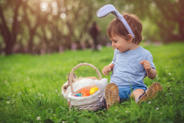 симпатичный маленький мальчик, играющий с кроликом и пасхальными яйцами - rabbit child pets little boys стоковые фото и изображения