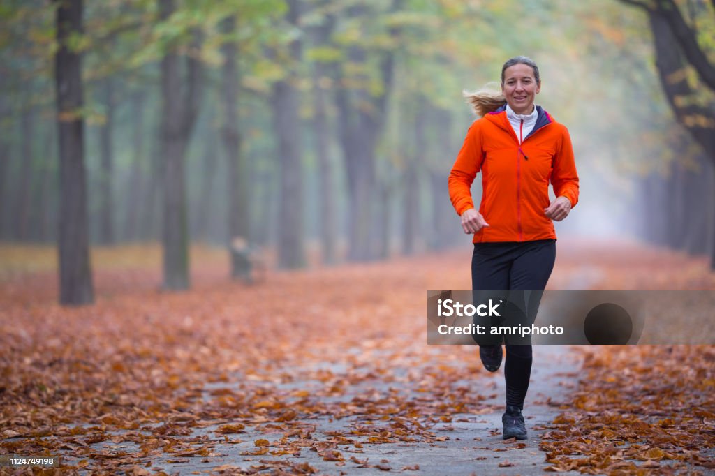 persone reali donna felice correre da sola nel parco la mattina d'autunno nebbiosa - Foto stock royalty-free di Autunno