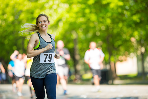 happy smiling young woman jogging at running event on sunny day in spring, shallow focus on female runner, background blurred