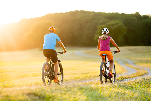 rear view two mountain bikers woman man cycling in rural landscape with electric bicycle on sunny summer day
