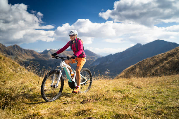 happy woman on electric mountain bike high up in european mountains smiling fit sporty woman cycling her electric mountain bike high up in mountains on sunny autumn day with white clouds mountain bike stock pictures, royalty-free photos & images