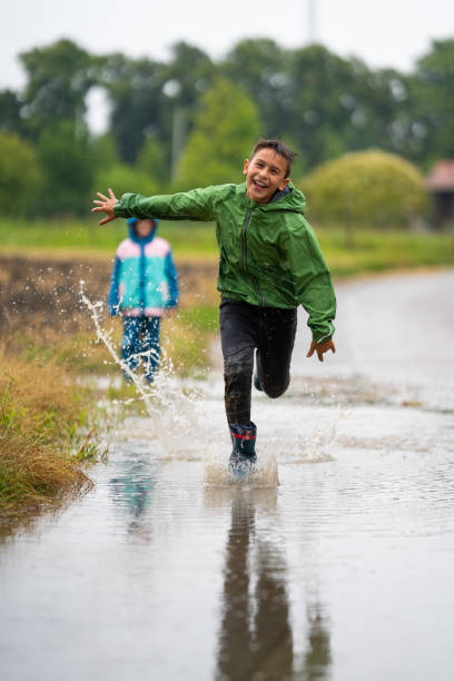 istock happy laughing boy running through water puddle in rain 1124750540