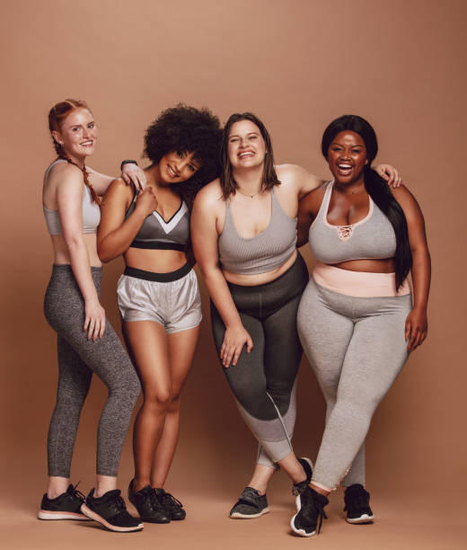 Lover your body Group of women of different race, figure type and size in sportswear standing together over brown background. Diverse women in sports clothing looking at camera and laughing. beauty in nature vertical africa southern africa stock pictures, royalty-free photos & images