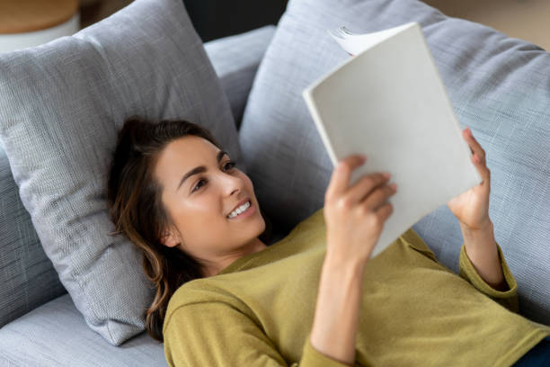 istock Happy woman reading a book at home 1124755486