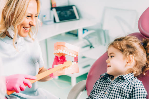 istock Smiling Dentist Brushing Dentures With Cute Girl In Office 1124764280