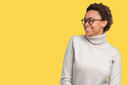 Young beautiful african american woman wearing glasses over isolated background looking away to side with smile on face, natural expression. Laughing confident.