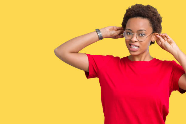 belle jeune femme afro-américaine portant des lunettes sur le fond isolé souriant tirant des oreilles avec des doigts, geste drôle. problème d'audition - casting glass photos et images de collection