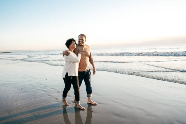 seniors hommes marchant avec femmes âgées sur la plage - holding hands couple senior couple togetherness photos et images de collection